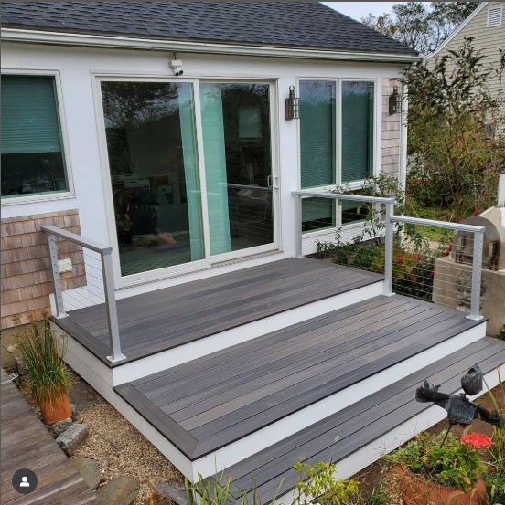 Modern gray Fiberon deck with sleek cable railing attached to a house with large glass doors and windows, surrounded by plants and a landscaped yard, conveying a clean and inviting outdoor living space